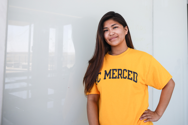 Female Student in Gold UC Merced t-shirt posing in front of a white board