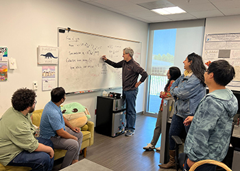 Six people in classroom setting reviewing something on whiteboard
