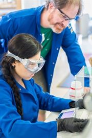 A student seated with a professor standing behind her in a chemistry lab.