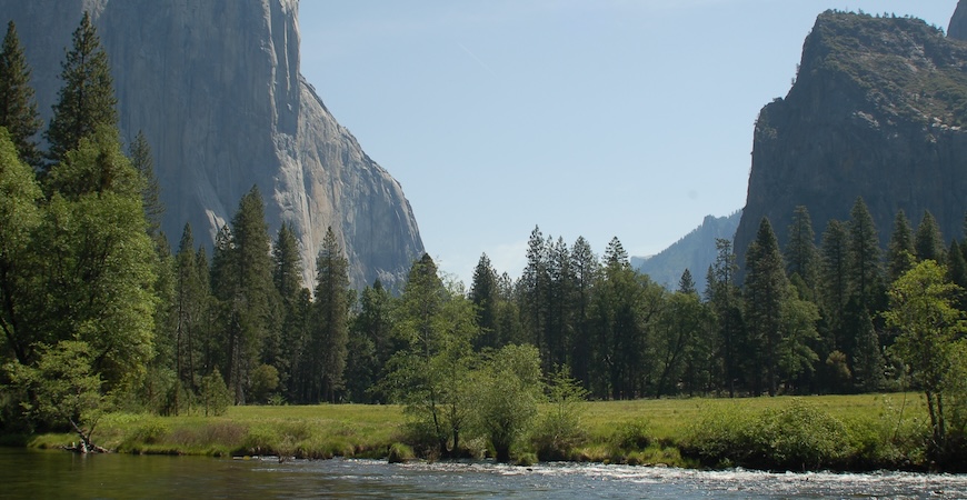 A scenic photo of water, a meadow and rock formations at Yosemite National Park. 