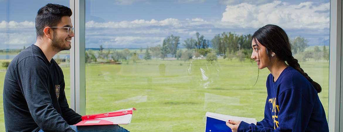 A male and female student study in front of a window with a beautiful, scenic backdrop.