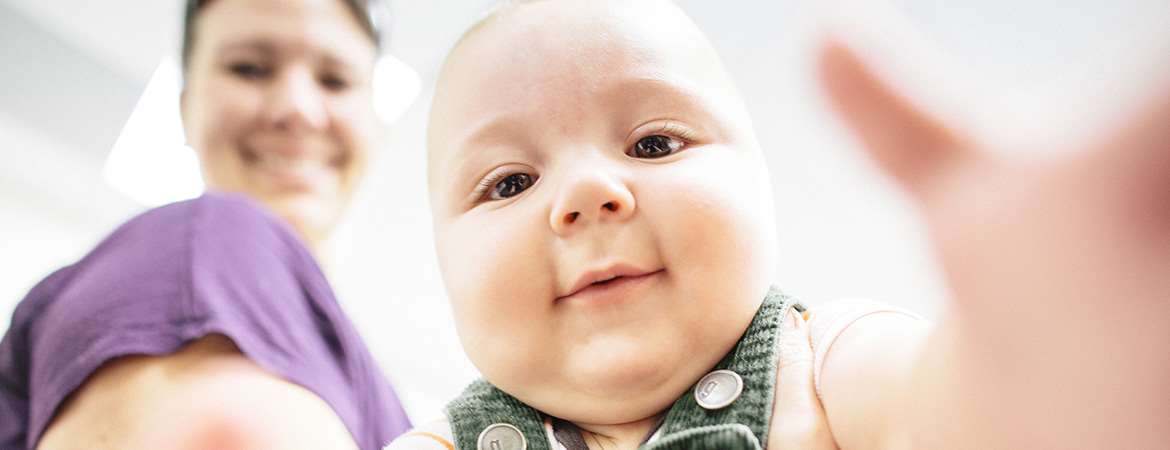 A woman holds a cute baby who is looking into the camera.