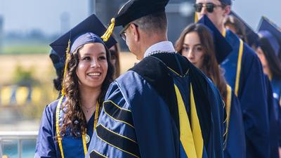 A student is congratulated by Chancellor Juan Sánchez Muñoz on the commencement stage.